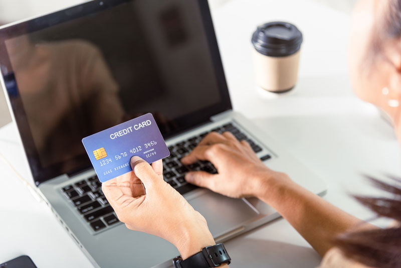 Woman hands holding credit card and using laptop with product purchase relying on PCI compliance.