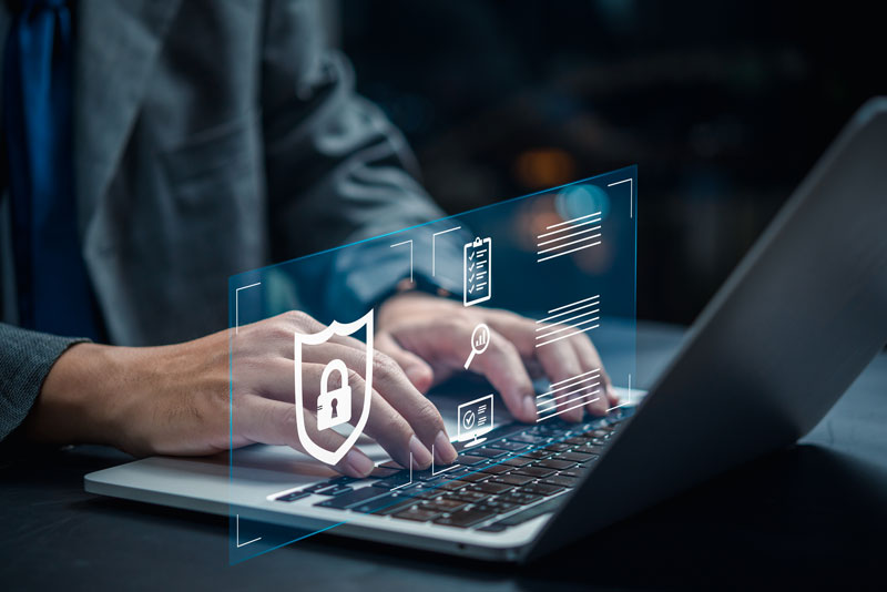 A man typing on a laptop with a graphic representing cybersecurity.