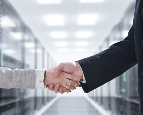 A businessman and businesswoman shaking hands in a server room.