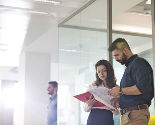 A man and a woman standing in an office reviewing some papers together.