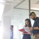 A man and a woman standing in an office reviewing some papers together.